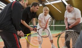 Mehrere blinde Tennisspieler stehen im Kreis und halten ihren Tennisschläger nach vorne.