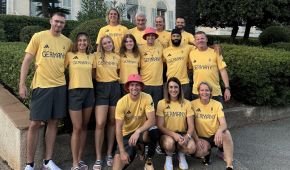 Auf dem Foto ist ein Teil der deutschen Para Leichtathlet*innen abgebildet, die im Trainingslager in Südfrankreich waren. Sie tragen gelbe Shirts und graue Hosen und haben sich vor einer Palme aufgereiht.
