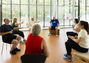 Menschen in einer Sportgruppe sitzen auf Stühlen und machen Übungen.