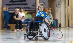 Kleines Mädchen holt beim Rollstuhltennis zum Schlag aus