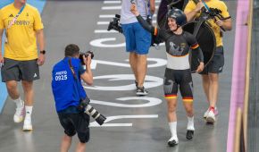 Im Pariser Velodrome läuft Maike Hausberger im Rad-Anzug neben der Bahn. Sie streckt lachend die Faust in die Höhe, während ein Fotograf die Linse draufhält.