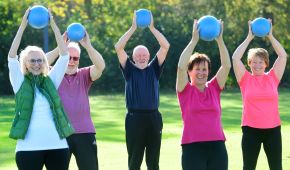 Rehasport: 5 Menschen auf einer grünen Wiesen, die jeweils einen Ball in die Höhe strecken