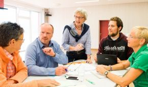 Fünf Personen sitzen um einen Tisch und tauschen sich angeregt aus