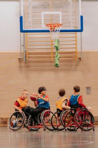 Vier Kinder spielen in einer Turnhalle Rollstuhlbasketball