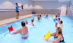 Eine Übungsleiterin zeigt Bewegungen am Beckenrand, die die Teilnehmer im Wasser umsetzen