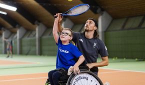 Trainer Niklas Höfken führt die Hand eines Jungens im Rollstuhl um einen Schlag auszuführen