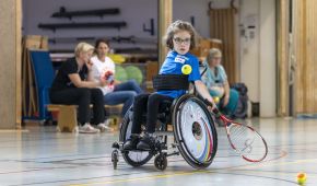 Kleines Mädchen holt beim Rollstuhltennis zum Schlag aus