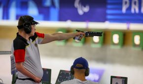 Para Sportschütze Tobias Meyer nimmt Maß und zielt auf die Scheibe bei den Paralympics 2024. Die Waffe ist in der linken Hand, die rechte Hand hat er an der Hüfte.
