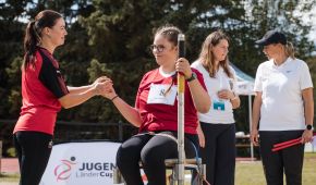 Szene beim Jugend-Länder-Cup: Ein Mädchen, reicht einem anderen Mädchen, das auf einem Wurfstuhl sitzt, die Kugel.