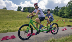2 Personen auf einem Tandem vor einer Wiese