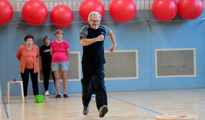 Ein Mann läuft durch die Turnhalle, im Hintergrund stehen drei Frauen