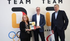 laudia Wagner gemeinsam mit Wolfram N. Diener und Werner M. Dornscheidt steht sie vor den Team D Logos und hält eine Plakette mit der Aufschrift: "Gemeinsam am stärksten" in die Kamera.