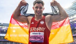 Felix Streng lacht und spannt seine Muskeln an. In den Händen hält er eine Deutschlandfahne hinter seinem Rücken.