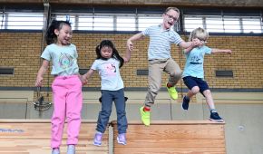 Vier Kinder springen Hand in Hand von einem Turnkasten