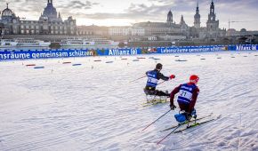 Zwei sitzende Athleten fahren vor den Wahrzeichen Dresdens im Sprint-Rennen