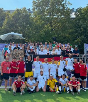 Mannschaftsbild der deutschen Blindenfußballer mit den Fans auf der Tribüne im Rücken