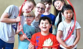 Gruppenfoto von lachenden Kindern beim Sport, die sich um einen Reifen versammeln und teilweise hindurchschauen