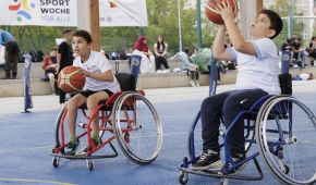Zwei Jungen im Rollstuhl haben ein Basketball in der Hand. Der Junge im Vordergrund setzt zum Wurf an