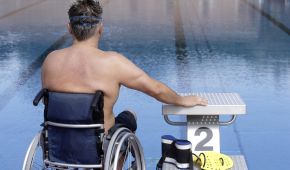 Ein Mann im Rollstuhl sitzt neben dem Startblock und schaut auf das Schwimmbecken