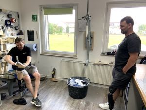 Heinrich Popow steht in der Werkstatt, ein Kollege arbeitet an einer Beinprothese