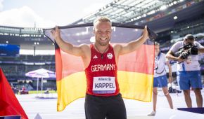 Niko Kappel strahlt mit der deutschen Fahne im Rücken übers ganze Gesicht. Im Hintergrund sieht man das lila Stade de France.